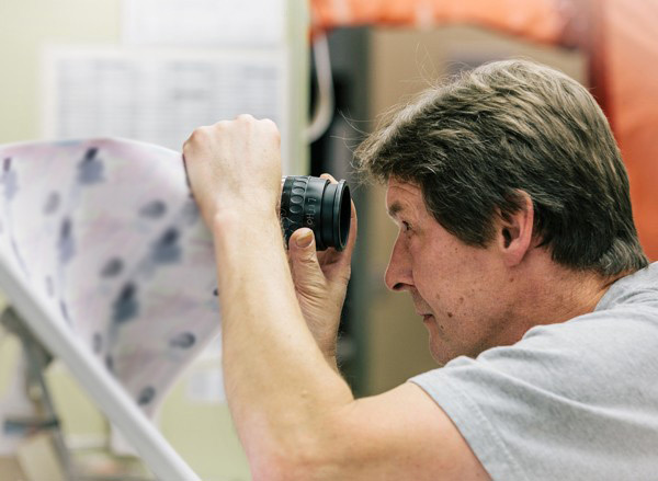 CBN employee looks at sheet of currency with looking glass